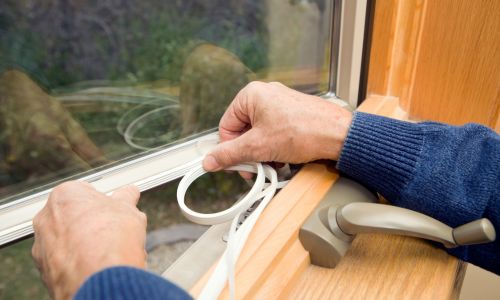 Homeowner sealing gaps around a window to help prevent pests from entering before winter